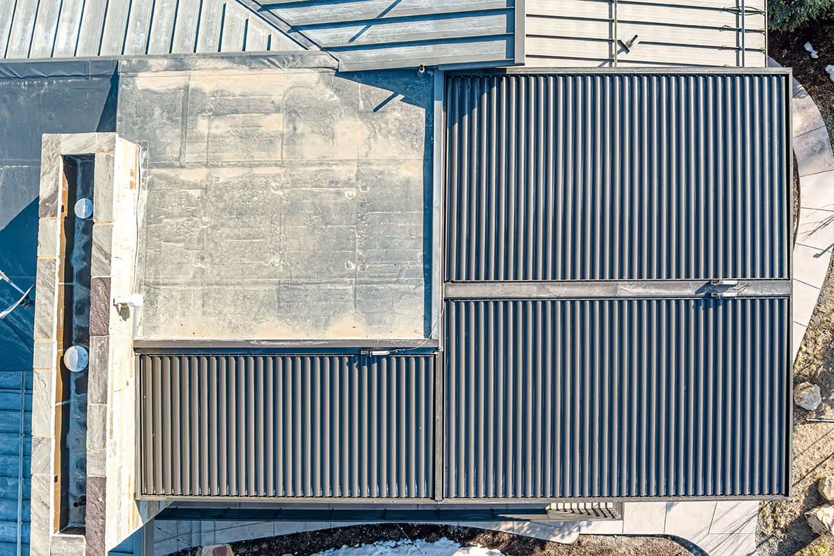 Aerial view of a modern, geometric roof with ribbed metal panels and stone textures. The design features sharp angles and contrasting materials.
